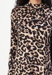Haut à manches longues avec col montant en imprimé léopard beige, marron et noir porté par une personne.