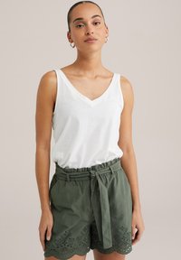 White sleeveless V-neck top paired with olive green shorts featuring a tied belt and scalloped hem with eyelet embroidery.