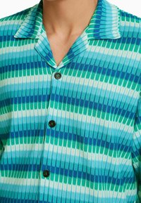 Stickad skjorta med knappar som har ett randigt mönster i olika nyanser av blått och grönt, med krage och fyra svarta knappar.