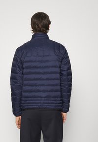 Vadderad marinblå jacka med hög krage, med ett kviltat mönster och elastisk nederkant. Baksidan har en slät yta utan dekorationer.