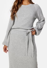 Pull en mailles côtelées gris avec manches longues et taille ceinturée, présentant un col rond et un tissu texturé.