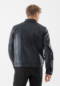 Giacca nera in pelle con un design strutturato, caratterizzata da un colletto classico, una trama liscia e dettagli di cucitura sottili sulla schiena.