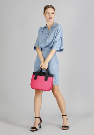 Borsa a tracolla rosa e nera con superficie texturizzata, manici corti e chiusura con zip, tenuta da un modello in un vestito di jeans su uno sfondo neutro.