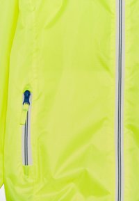 Veste légère jaune fluorescent avec fermeture éclair sur le devant, tissu texturé et accent de tirette de fermeture éclair bleue.
