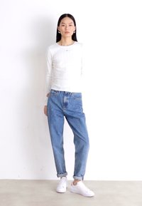 Hvid ribbet langærmet top parret med lyseblå baggy jeans, oprullet ved manchetterne, komplementeret af hvide sneakers. Enkelt design og farvepalet.