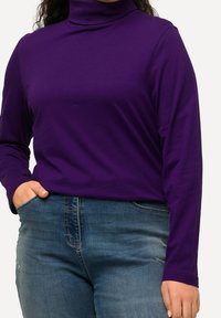 Lila långärmad polokraga topp i mjukt material, parat med blå denimjeans med en lätt sliten look.