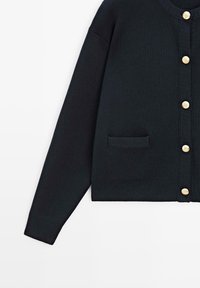 Sort langærmet cardigan med guldknapper foran og en lille lomme på venstre side.