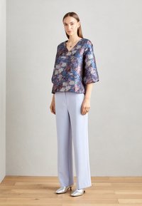 Haut à motifs floraux avec des manches évasées dans des nuances de violet et de bleu, associé à un pantalon large lavande clair et des talons argentés. Texture lisse.