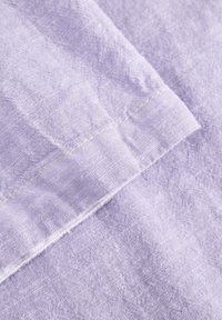 Tessuto di lino di colore lavanda chiaro con una finitura testurizzata. Presenta un bordo rifinito con cuciture visibili di un colore chiaro a contrasto.