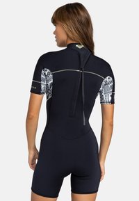 Combinaison de plongée noir à manches courtes avec des accents blancs à motifs sur les manches, fermeture éclair au dos et texture lisse pour les activités aquatiques.