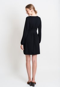 Abito nero con maniche lunghe, vita aderente e gonna svasata. Tessuto morbido con un design semplice. Indossato con scarpe con tacco a blocco marroni.