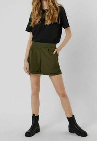 Czarna koszula z krótkim rękawem, oliwkowo-zielone szorty z dwoma bocznymi kieszeniami oraz czarne botki na grubej podeszwie.