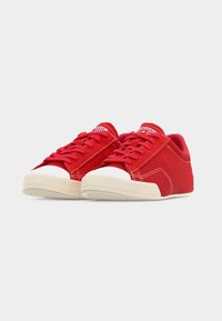 Ζευγάρι κόκκ ινα αθλητικά παπούτσια χαμηλού ύψους με λευκές λαστιχένιες μύτες και σόλες, με κόκκινα κορδόνια και εμφανείς λεπτομέρειες ραφής.