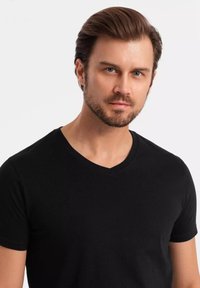 Camiseta negra de algodón con un diseño ajustado, que presenta un escote en V y mangas cortas, mostrada sobre un fondo neutro.
