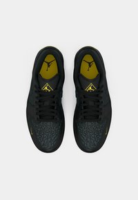 Sneaker nere con sovrapposizioni grigie scure strutturate, lacci neri e un accento giallo sul tallone. L'interno presenta un logo nero e giallo.