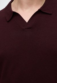 Gros plan d'une personne portant une chemise bordeaux foncé avec un col et un décolleté en forme de V.