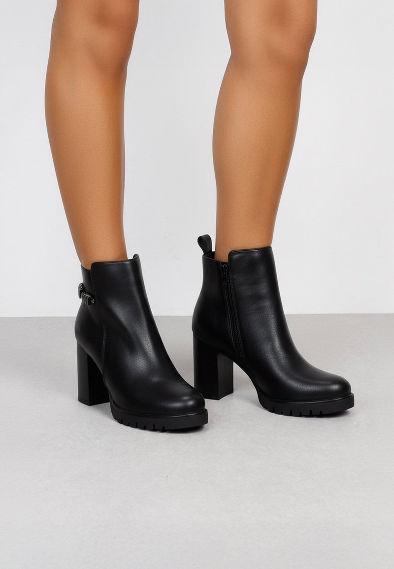 Botines negros de tobillo con un acabado de cuero liso, tacones cuadrados, cremalleras laterales y suelas texturizadas para mayor agarre.