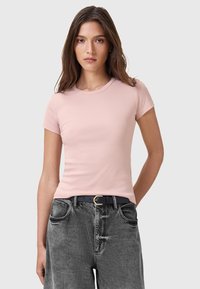  Lichtroze aansluitend T-shirt met korte mouwen en een ronde halslijn, gecombineerd met hoogopgesneden vervaagde zwarte jeans en een zwarte riem met een gouden gesp.