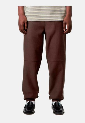 Pantalon marron foncé ample porté avec des mocassins noirs et des chaussettes blanches, associé à un haut rayé visible à la taille.