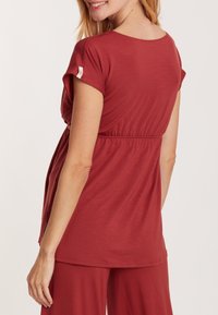 Rotes, kurzärmliges Oberteil mit gerafftem Taillenabschluss. Hergestellt aus weichem, dehnbarem Material für maximalen Komfort. Leicht und mit lockerer Passform.
