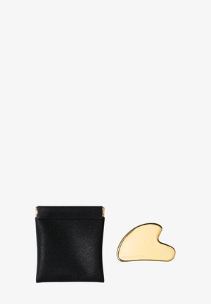Zwarte faux leren pouch met gouden hardware, gecombineerd met een gouden sculptuurtool met de inscriptie "REVOLUTION."