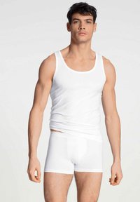 Un débardeur en coton blanc et un shorty sur un modèle, présentant un design ajusté, une texture lisse et un style simple et dépouillé.