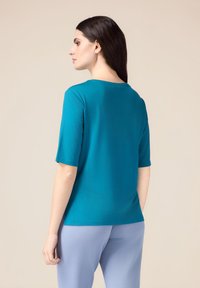 Top de manga corta en color verde azulado con un escote redondo, que presenta una textura suave y un corte relajado, combinado con pantalones azul claro.