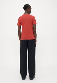 Raudona trumpa rankovėmis medvilninė marškinėliai, derinami su juodomis plačiomis kelnių. Matoma prisitaikanti ir lygi tekstūra, su paprastu apvaliu kaklu.