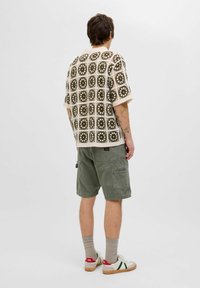 Kortærmet skjorte med en cremefarvet bund og et olivengrønt firkantet mønster. Kombinationen med grønne cargo-shorts og hvide sneakers.