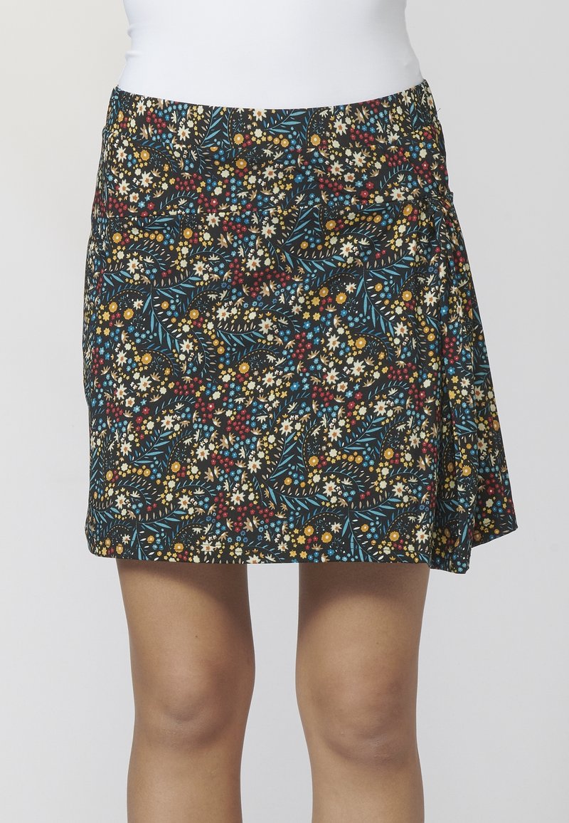 Jupe mini florale noire avec de petites fleurs jaunes, rouges, bleues et blanches, portée avec un haut blanc, vue de la taille aux genoux.