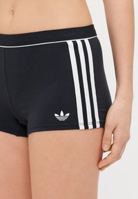 Calças de atletismo pretas feitas de material elástico, com um design de três riscas brancas nas laterais e um pequeno logotipo branco na bainha.