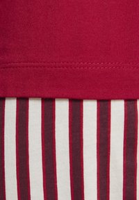 Nahaufnahme einer roten Stoffnaht über vertikalen Streifen in Weiß, Dunkelrot und Rot auf strukturiertem Textil.