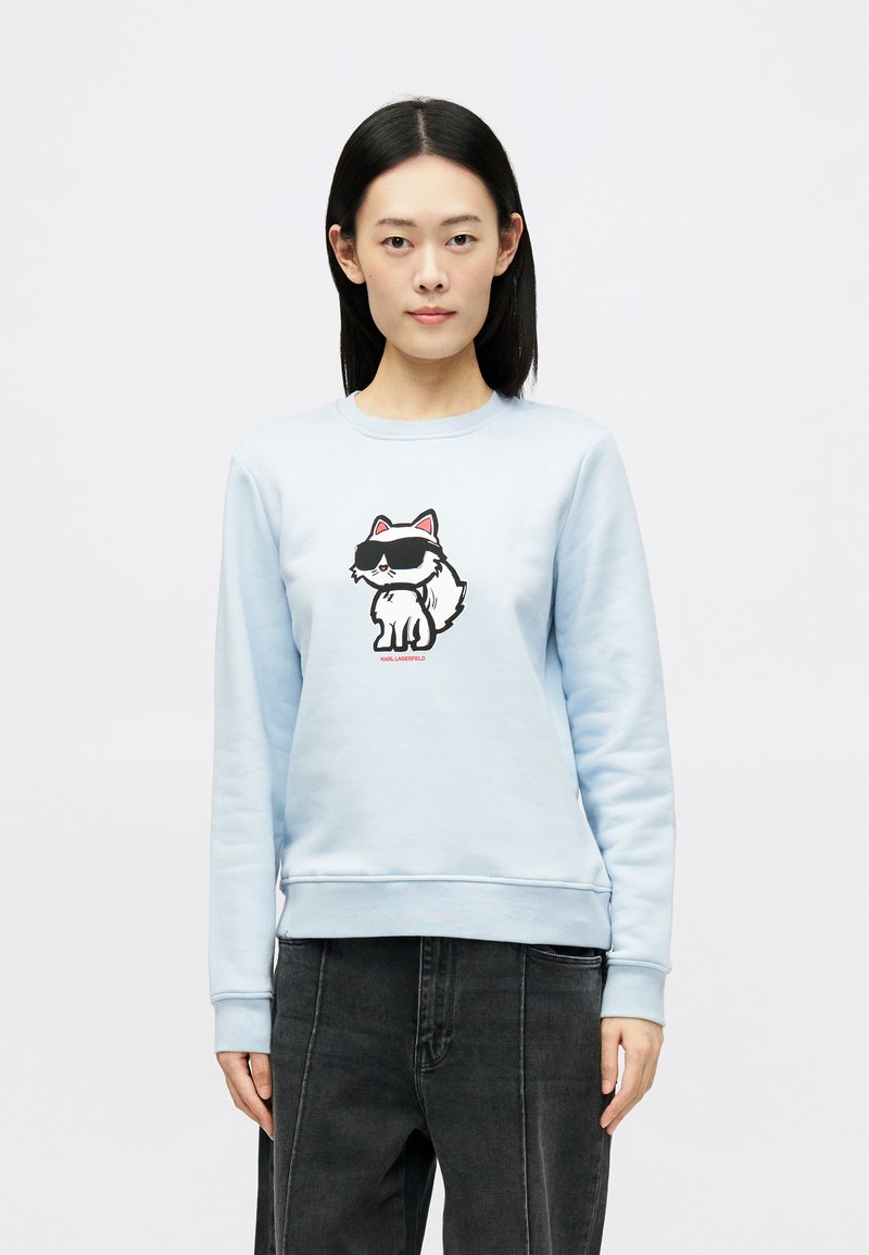 Sweatshirt azul claro em tecido macio, com uma impressão de um gato de cartoon a usar óculos de sol na parte da frente. Punhos e barra canelados. Corte casual.