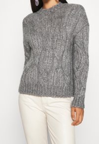 Šedý svetr s pleteným vzorem, kulatým výstřihem, žebrovanými manžetami a spodním lemem, s texturovaným vzorem a mírně volným střihem.