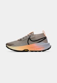 Beige og oransje Nike ZoomX terrengløpesko med svart swoosh, perforert overdel, Vibram såle og bakre trekksnor.