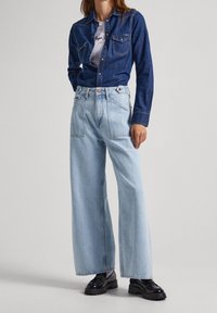 Ljust blå vida jeans i denim, med hög midja, fram- och bakfickor samt sömsyningar. Matchas med en mörk denimskjorta.