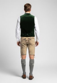 Groene fluwelen vest, witte shirt, beige korte broek met decoratieve stiksel, grijze kniehoge sokken en bruine schoenen. Gezicht vanuit de achterkant.