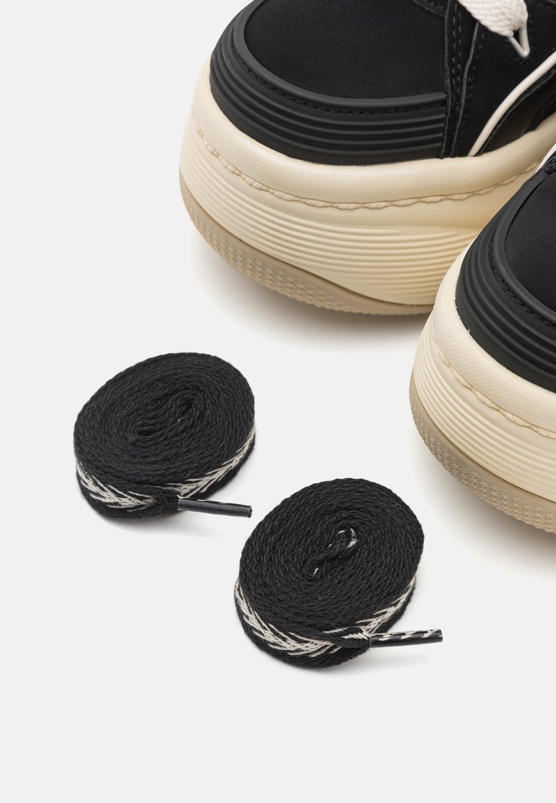 Sneakers platform nere e crema con suola in gomma, dotate di spesse stringhe nere e dettagli testurizzati. Include due stringhe nere arrotolate con strisce bianche.