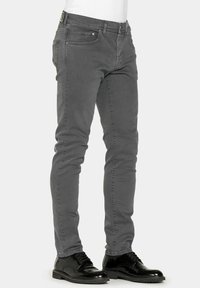Jeans grigi slim-fit con una leggera elasticità, dotati di cinque tasche e dettagli di cucitura discreti, abbinati a scarpe in pelle nere.