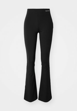 Leggings neri a campana realizzati in tessuto elasticizzato, con un alto elastico in vita e un piccolo logo bianco sul davanti. Texture liscia.