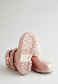 Rosa Kunstlederstiefel mit einem flauschigen Innenfutter und Schnallendetails; strukturierte Gummisohle mit einem Sternmuster für besseren Halt.