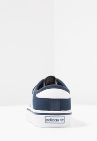 Marinblå canvas sneakers med en vit gummisula, vit hälaccent och logotyp på sidan; har en strukturerad, sydd design.