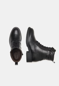 Zwarte leren laarzen met een ronde neus, vetersluiting en studs. Voorzien van een gemêleerde zool en een aantrektasje op de hiel.