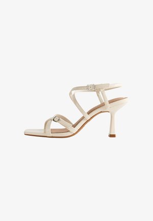 Sandalo con tacco beige con tre cinturini incrociati, fibbia regolabile e tacco a stiletto sottile. Materiale in finta pelle liscia, design con punta quadrata.
