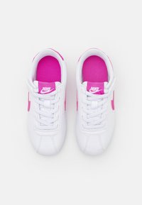Chaussures de sport blanches avec des accents roses, doublure en maille texturée, design à lacets traditionnel et logo Nike sur la languette et sur le côté.