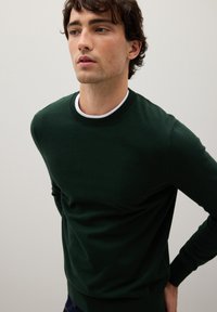 Dunkelgrüner Pullover aus weichem Material, mit einem klassischen Rundhalsausschnitt und langen Ärmeln, in taillierter Passform und mit gerippten Bündchen.