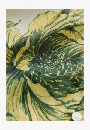 Floral-patterned fabric with green and yellow hues, featuring a soft texture and outlined flower designs. Includes a white button detail.