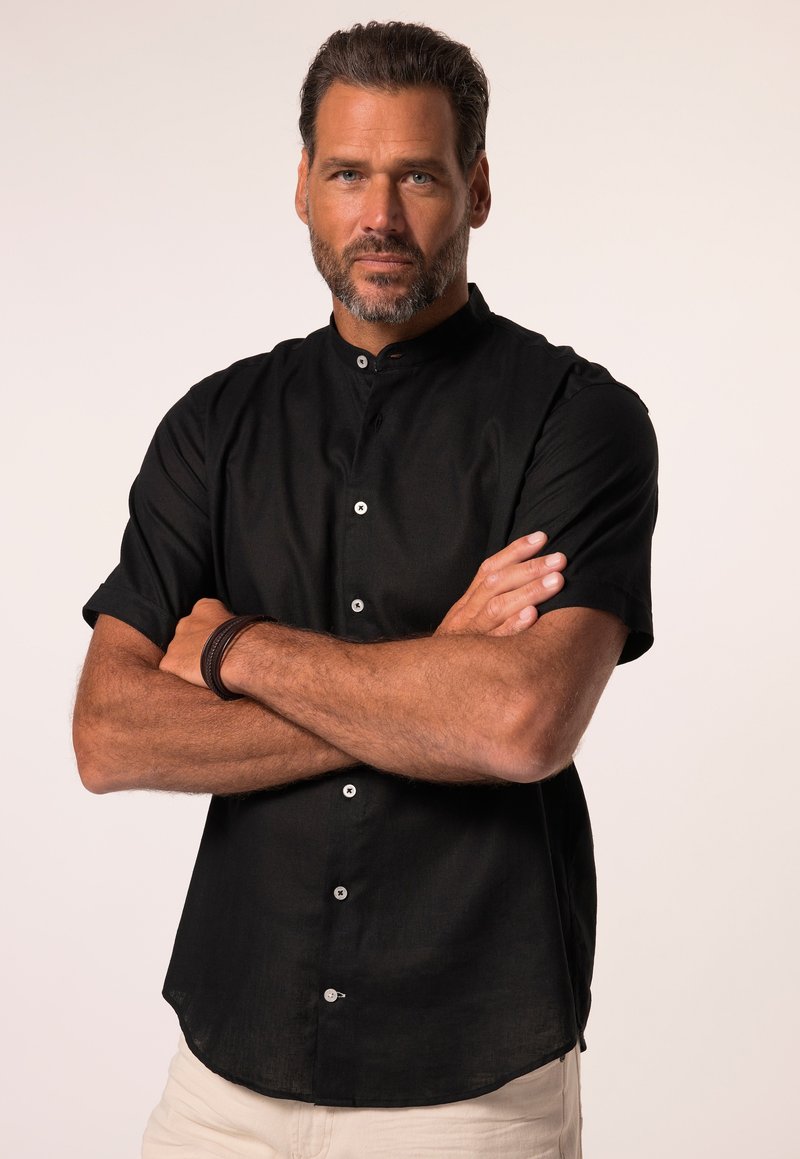 Mustat lyhyt hiha -paita, jossa on mandariinikaulus, etunappikiinnitys ja sileä pinta. Korostuksena valkoiset napit.