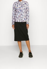Blomstret langærmet bluse i lilla, blå og gul på en lys baggrund, parret med en sort knælængde nederdel og kraftige sorte loafers.