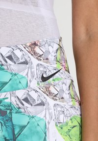 Nike athletic shorts with a diamond pattern in green, white, and silver. Features a black logo and smooth, stretchable fabric.